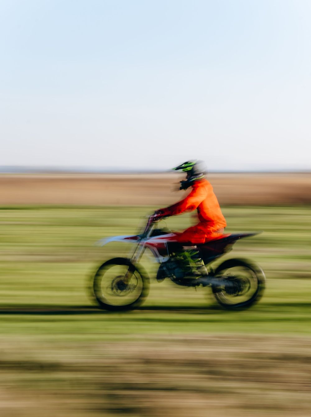 Motocross rider in orange gear speeding on a dirt bike across an open field with motion blur effect.
