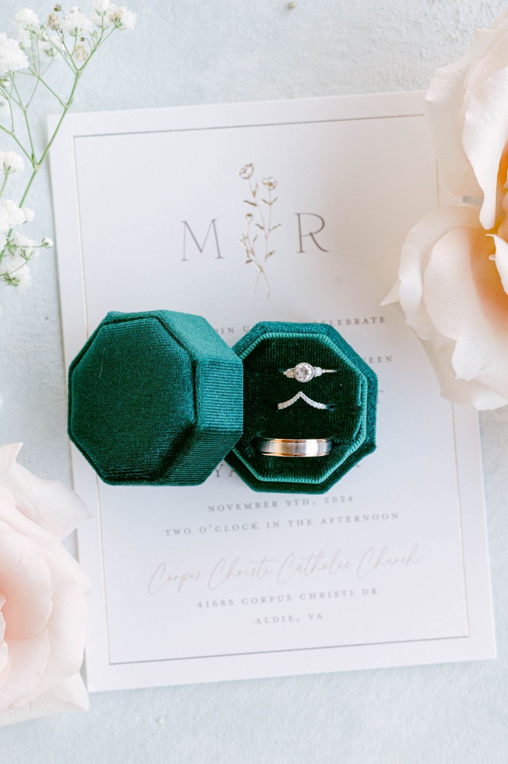 Wedding rings displayed in a green velvet octagonal box atop an elegant monogrammed wedding invitation.