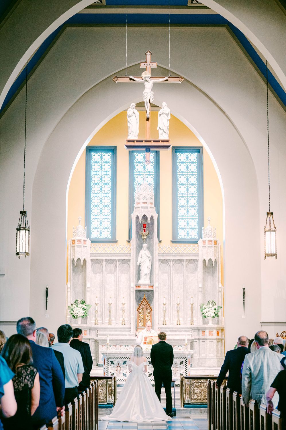 Bride and groom stand at the altar of an elegant Catholic church with arched ceilings and stained glass windows.