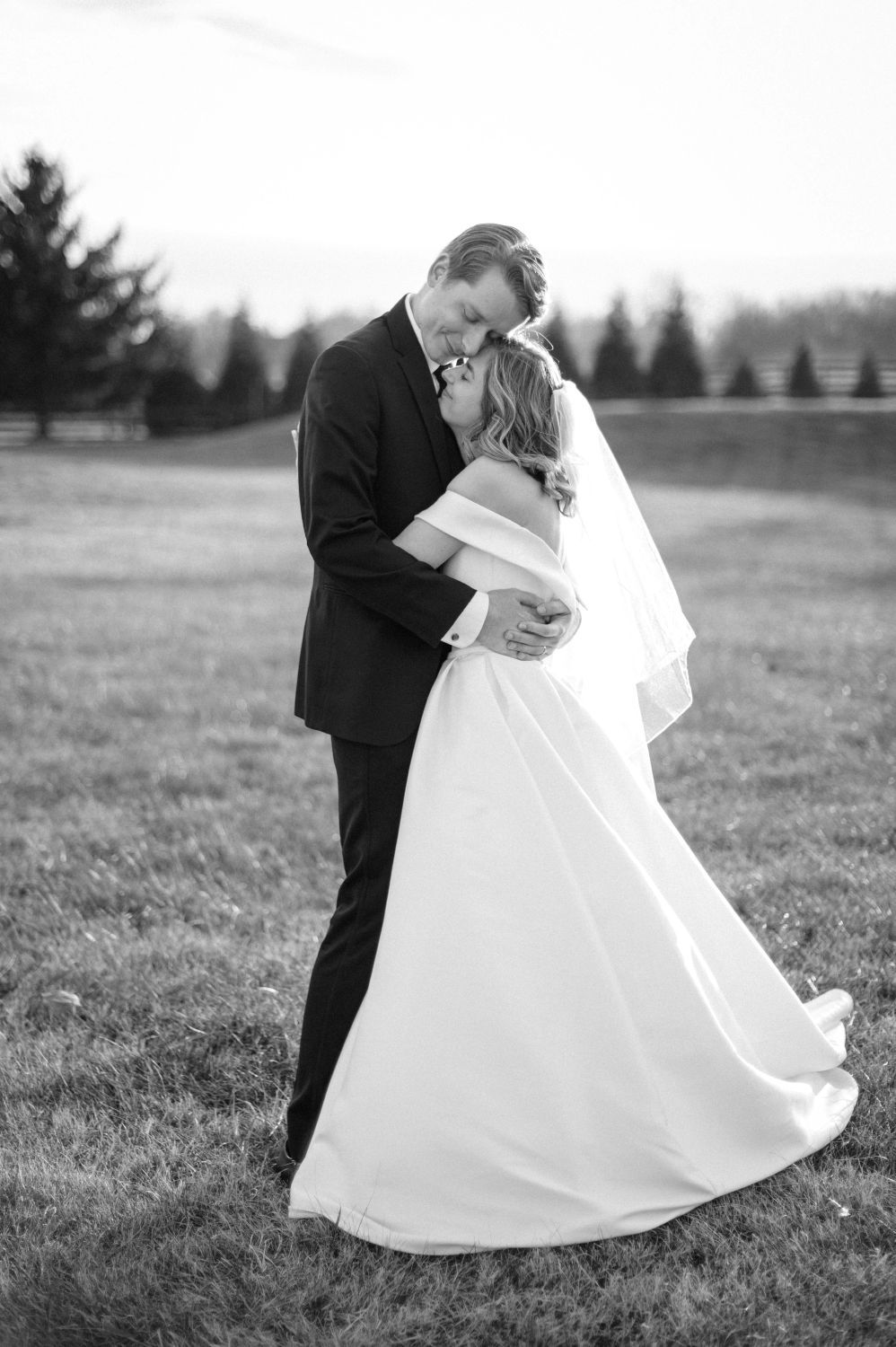 Black and white photo of bride and groom sharing a romantic kiss while embracing in an open field.