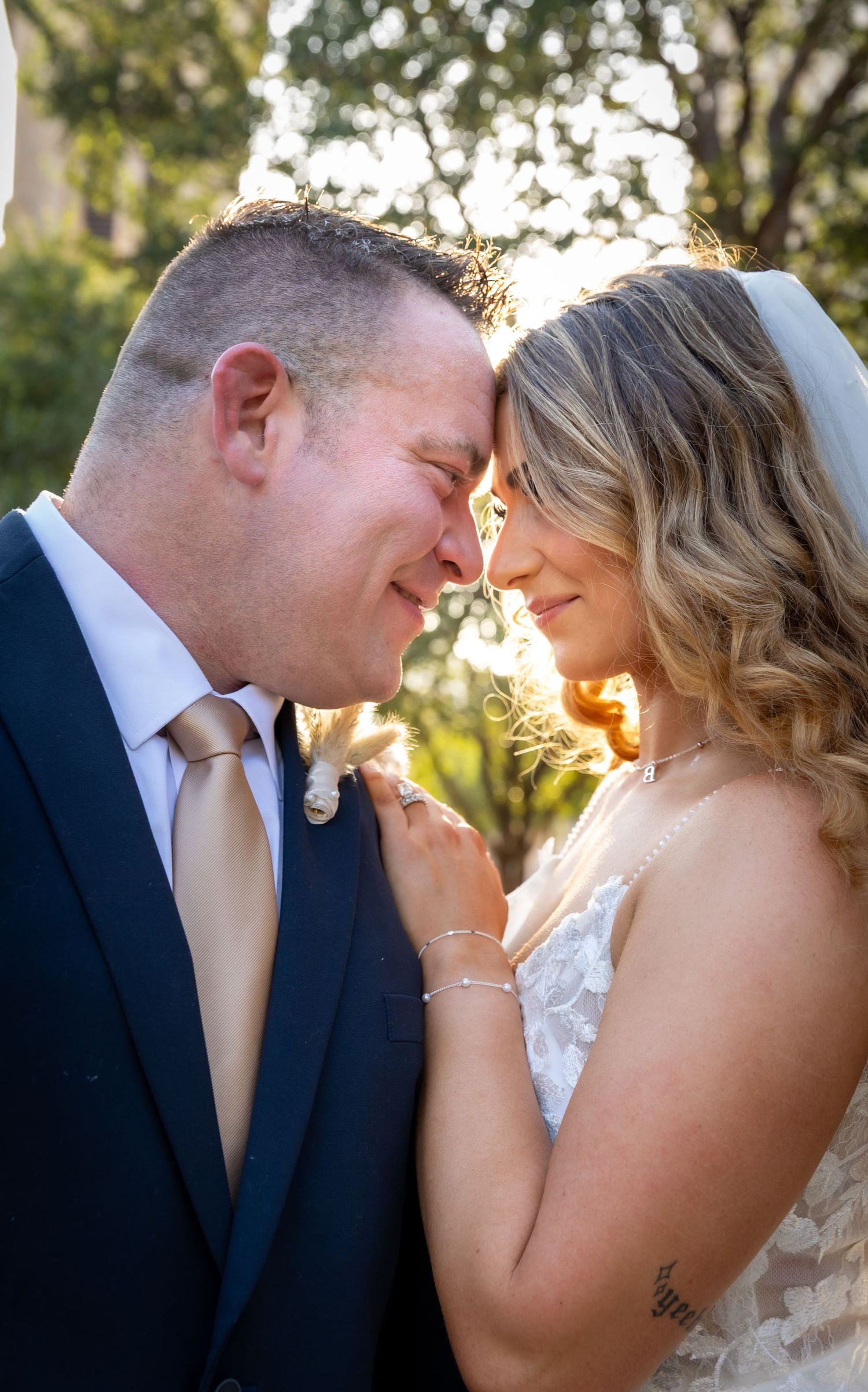 Bride and groom exchange rings during outdoor wedding ceremony with officiant in white robe and floral arch backdrop.