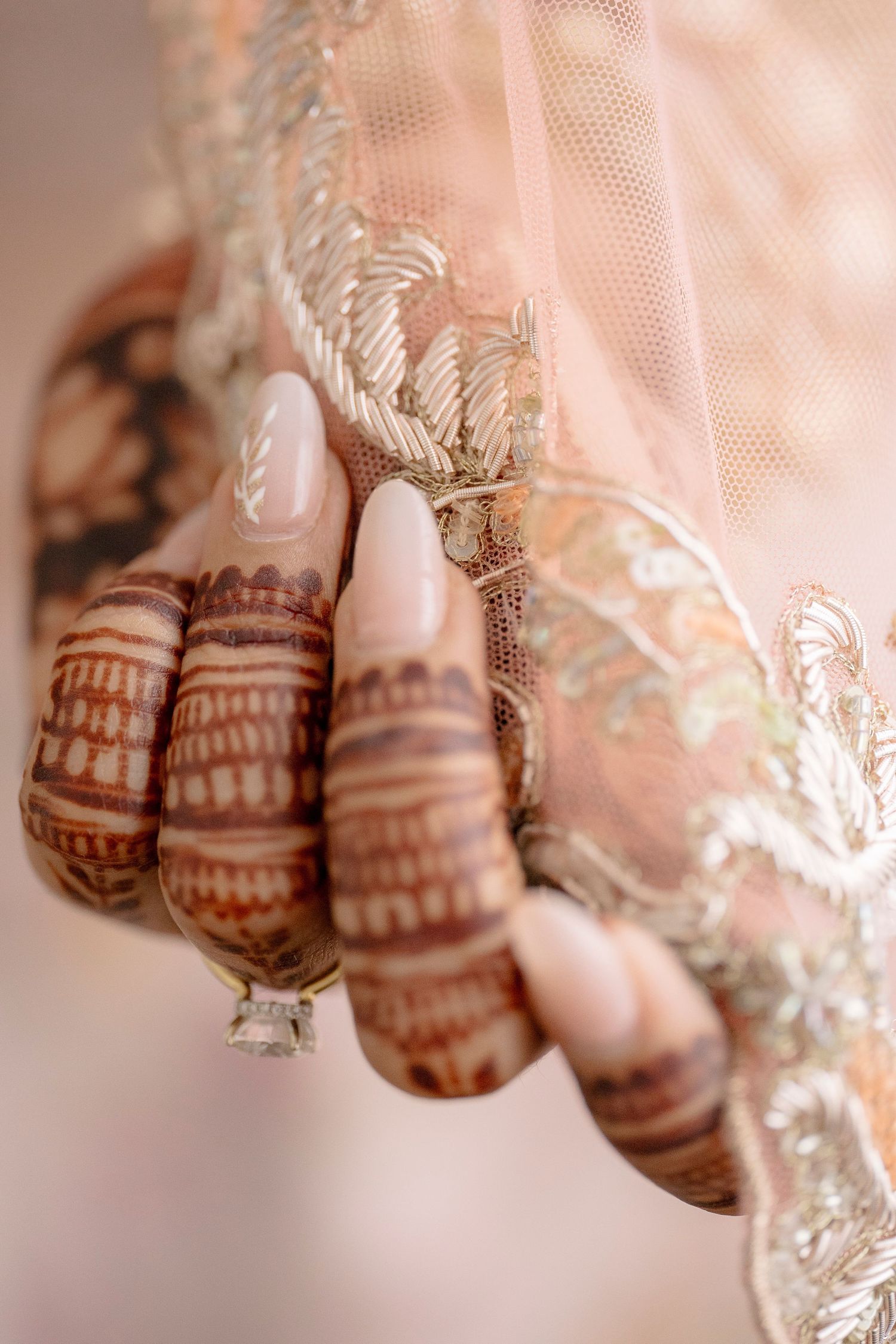 Close-up of bride's hands adorned with intricate henna mehndi designs, holding delicate lace fabric with silver embroidery.