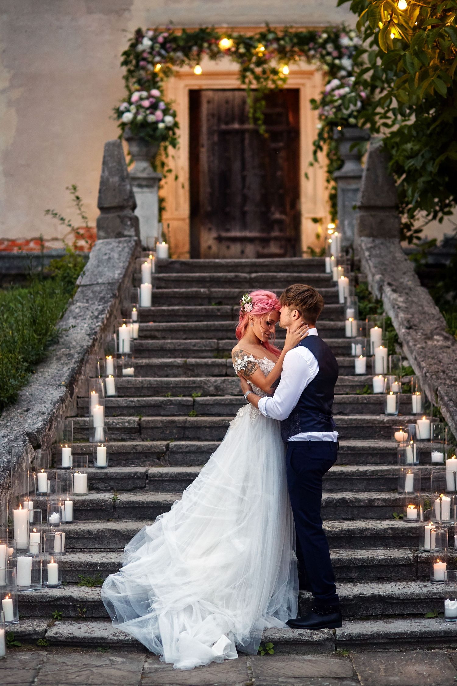 Les mariés s'enlacent sur un escalier de pierre éclairé aux chandelles, orné de fleurs et de guirlandes lumineuses, lors d'une cérémonie