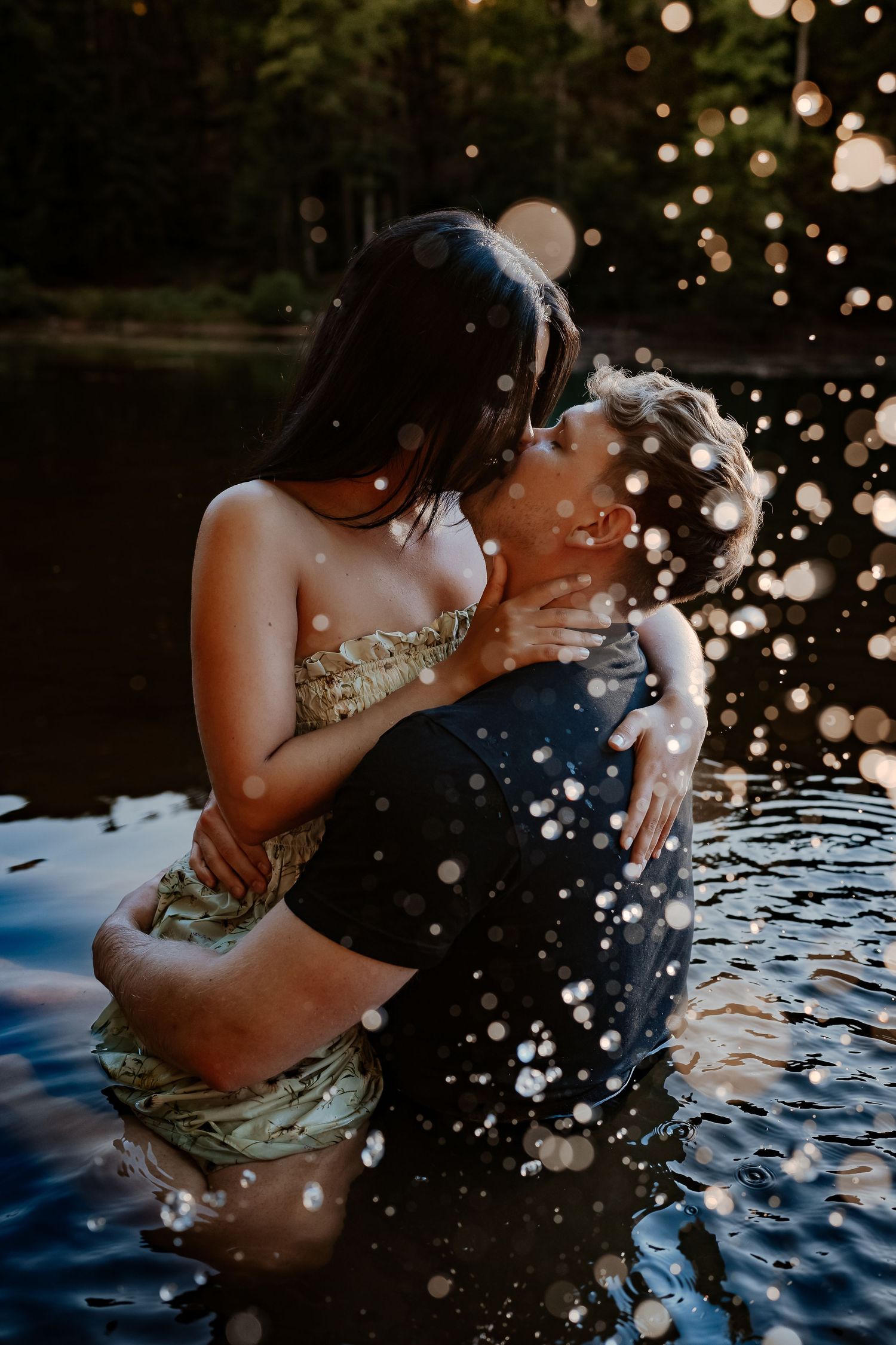 Couple sharing intimate moment in lake water with splashing droplets at dusk.