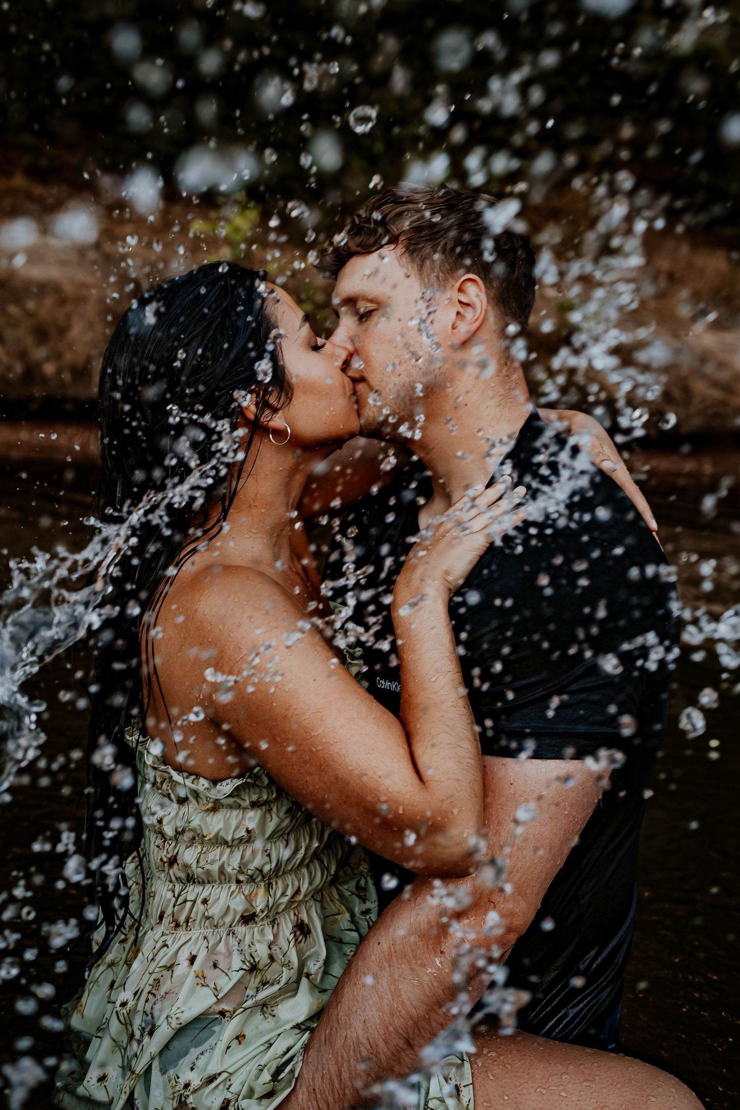 Passionate couple embracing in water with spray droplets creating magical atmosphere.