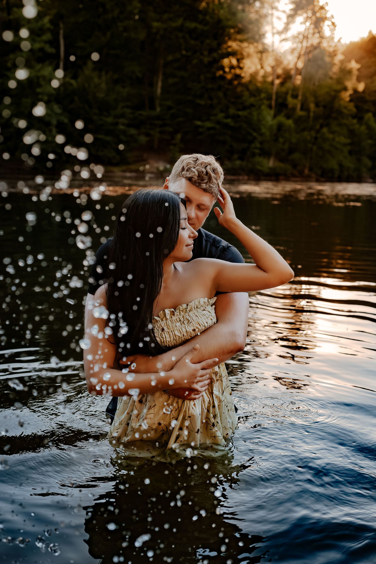 Couple splashing in a lake during golden hour with water droplets sparkling in the sunlight.
