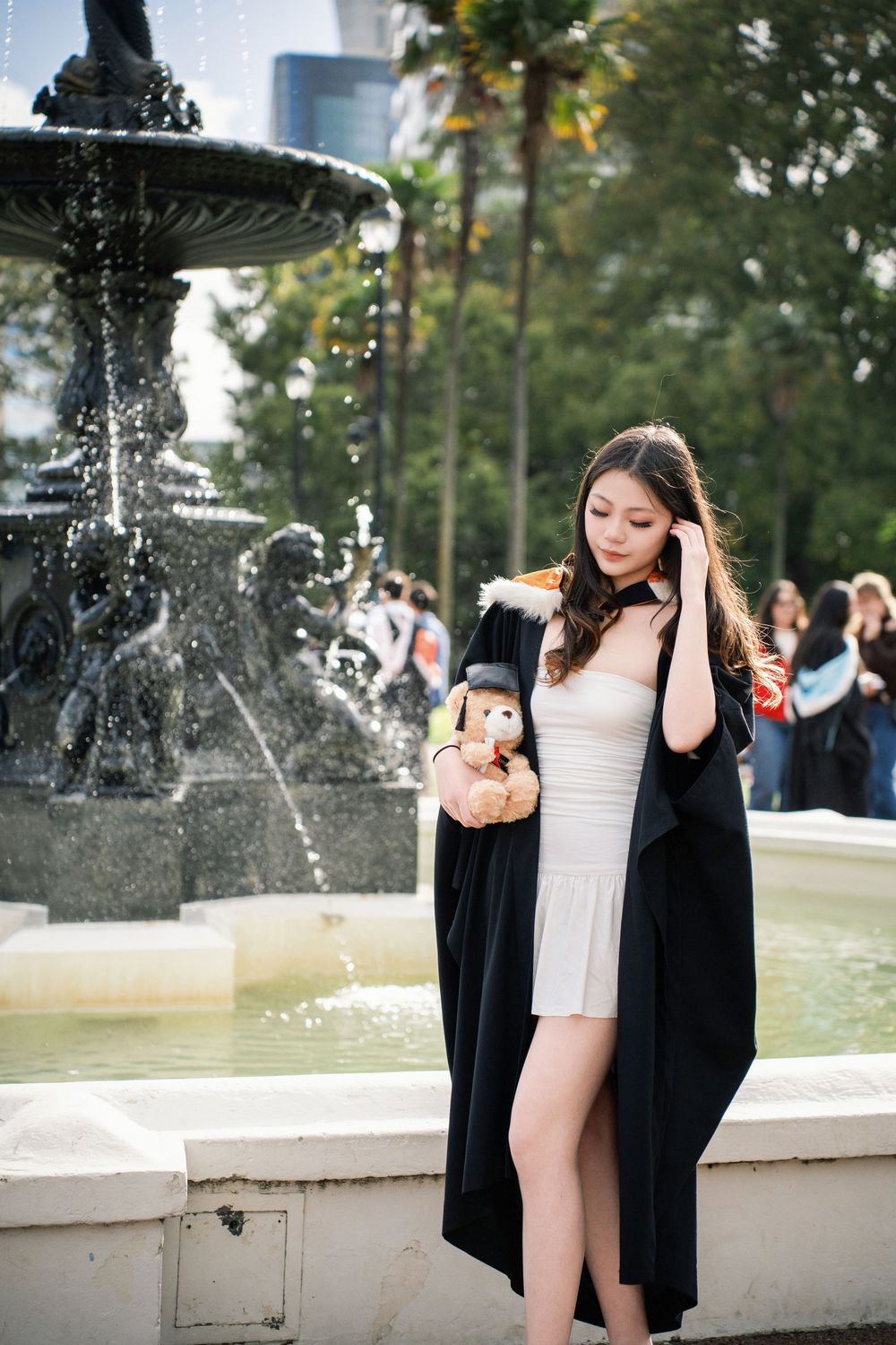 A graduate posing by a fountain in an Auckland albert park.