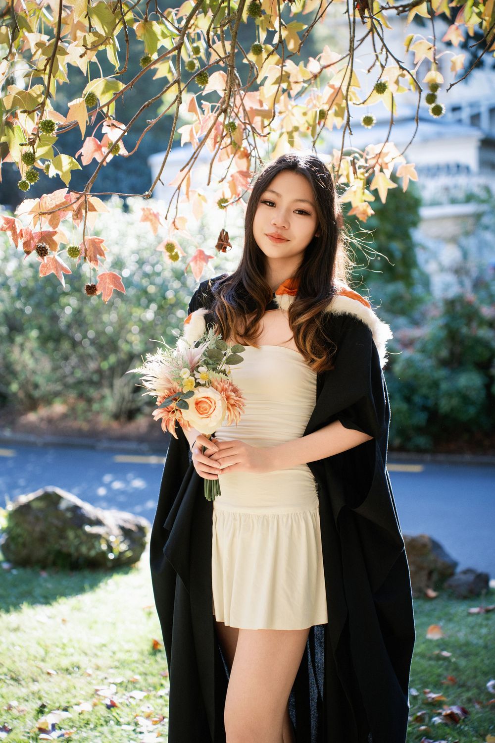 A graduate holding flowers in an outdoor Auckland campus garden.