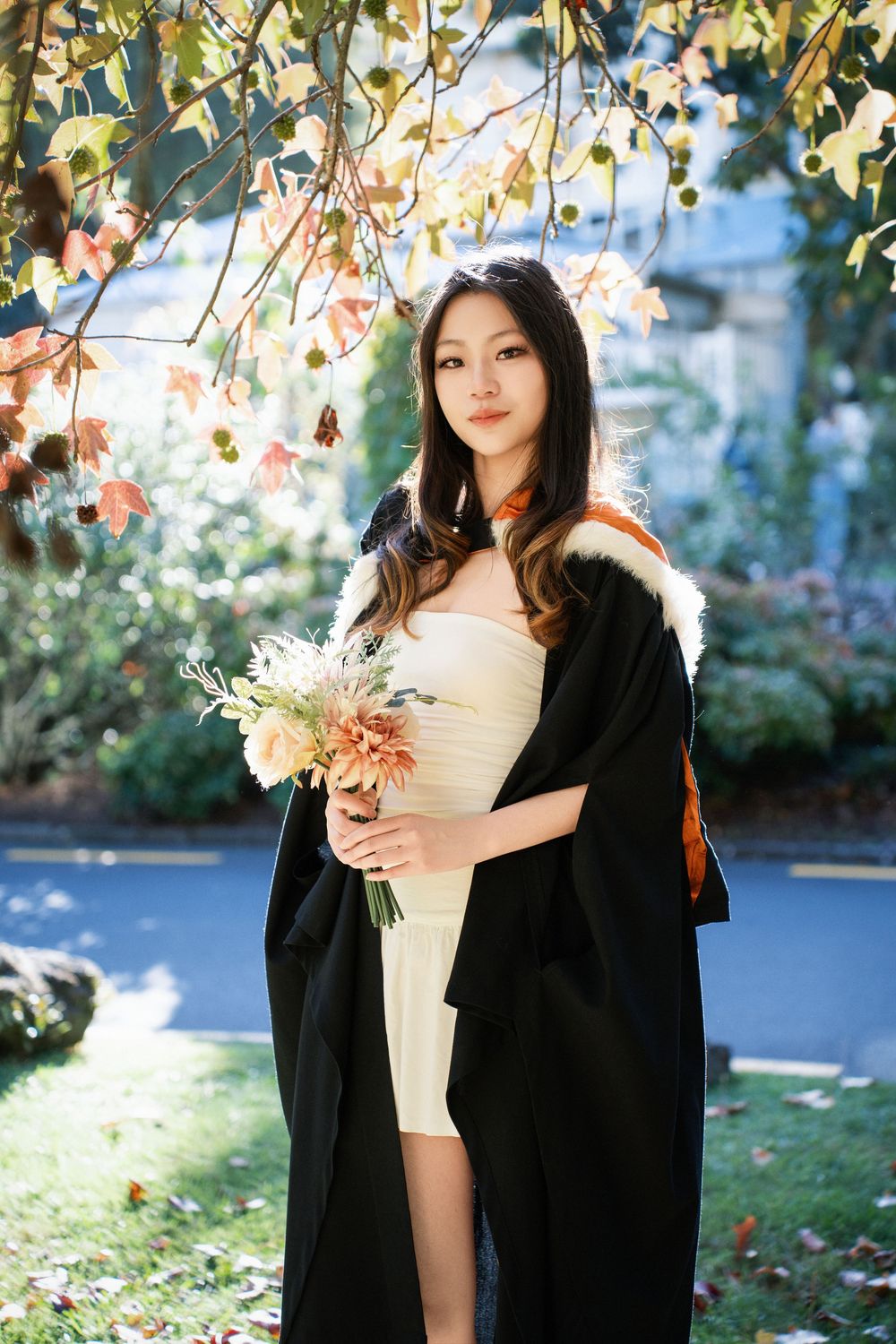 Graduation photography of a student in a lush, tree-filled outdoor campus setting in Auckland.