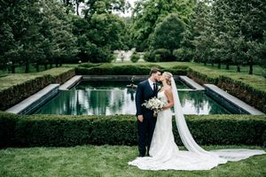 Bride and groom share a romantic moment in a formal garden with manicured hedges and a reflecting pool.