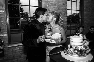 Black and white photo of bride and groom sharing a kiss while cutting their elegant wedding cake at reception.