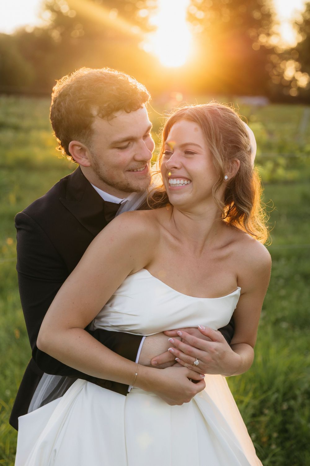 Bride and groom embracing at golden hour sunset in a green field, smiling joyfully on their wedding day in  Wisconsin