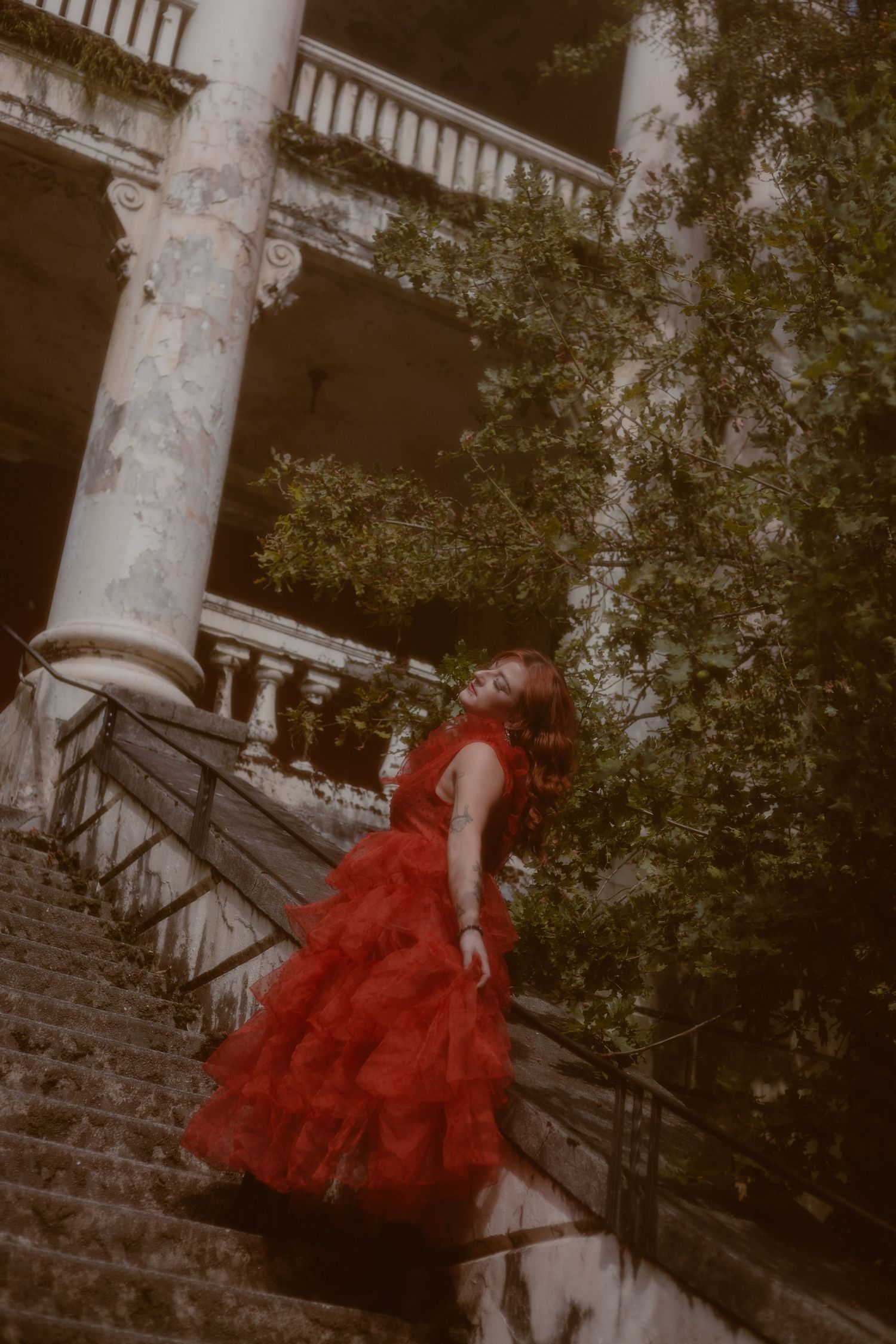 Moody portrait of client wearing a red dress while walking up the stairs of an abandoned asylum in British Columbia.
