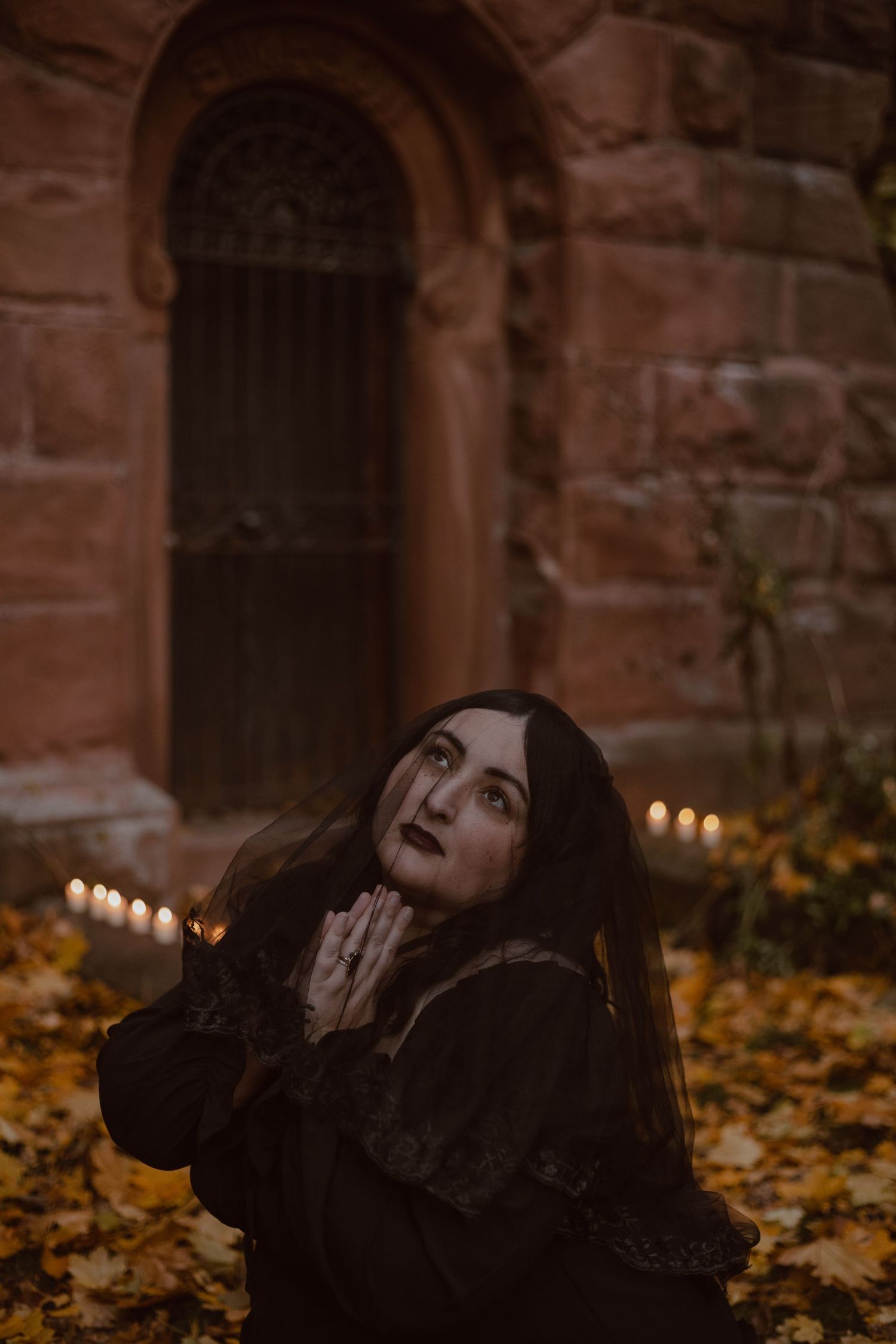 Branding portrait of Diana kneeling in front of candles and leaves. Her face covered with a black veil really gives it a gothic vibe.