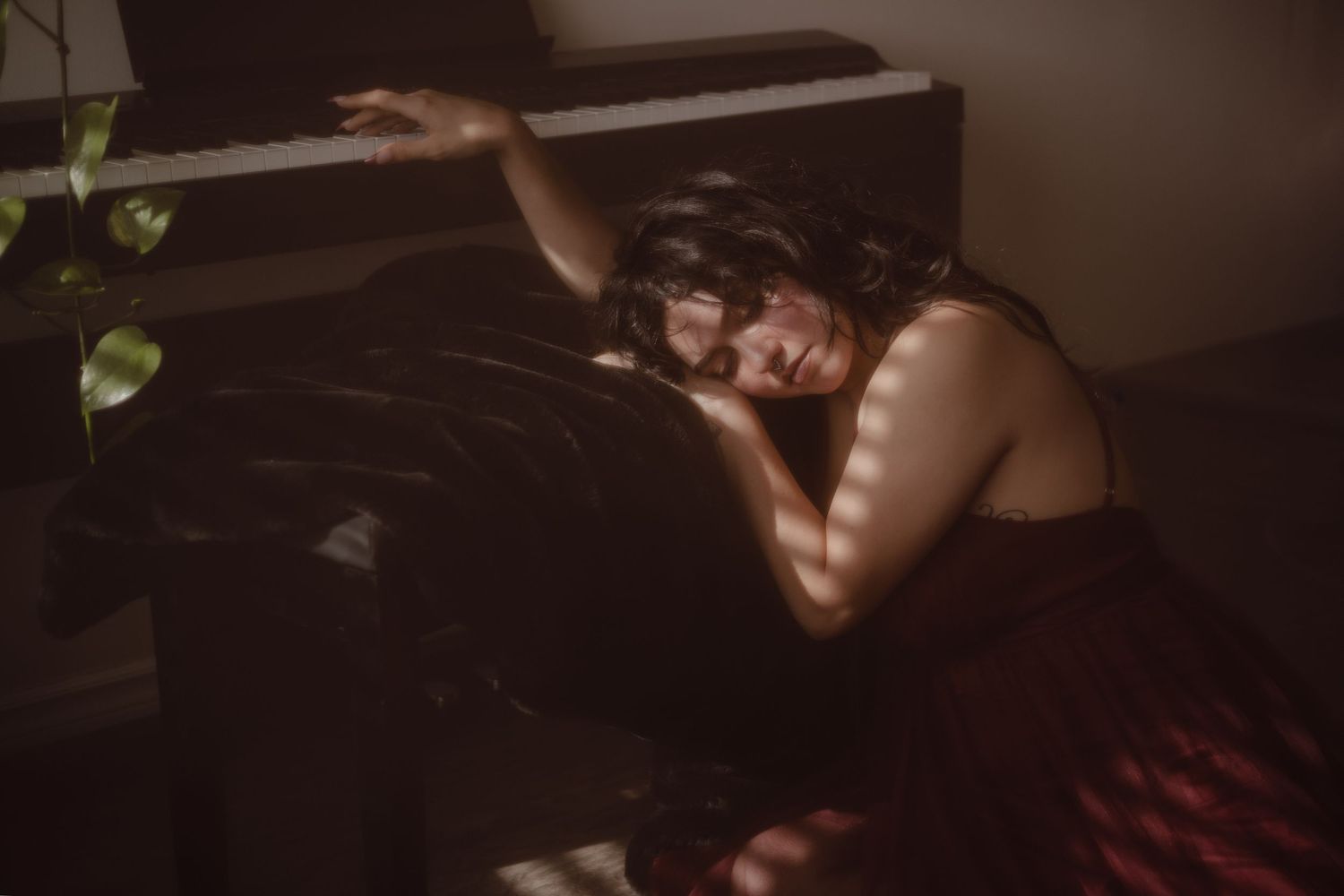 Soft light sneaks through the window during this portrait session while the model reaches over her piano.