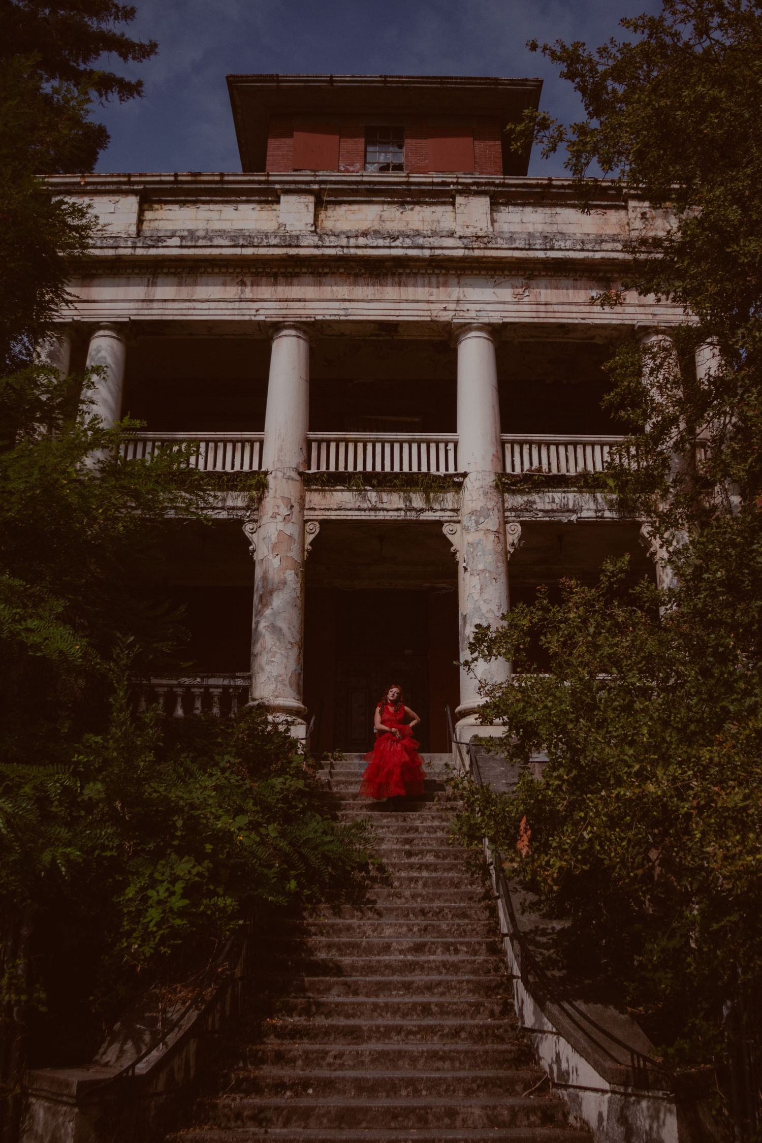 An establishing shot of model in red dress at Riverview Hospital in British Columbia. The photos from this session are eerie and moody.