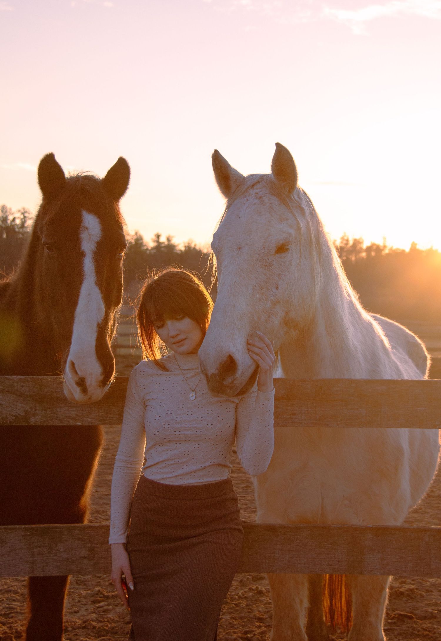 The model snuggles up between two horses at Green Acres farm in Hamilton, Ontario during golden hour.
