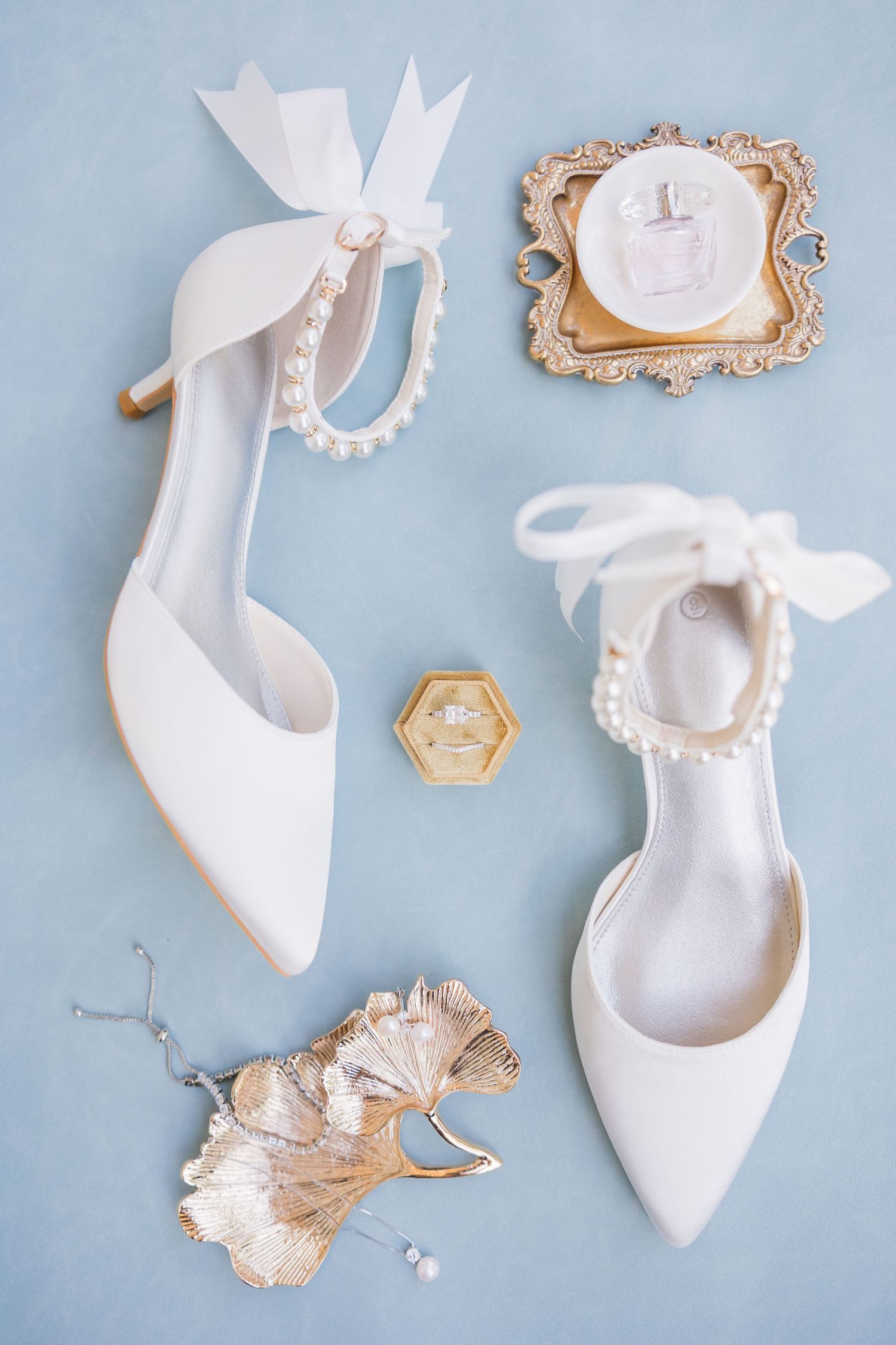 White bow heeled mules displayed on rustic wood with orange kumquats and a peach, elegant bridal shoe styling.
