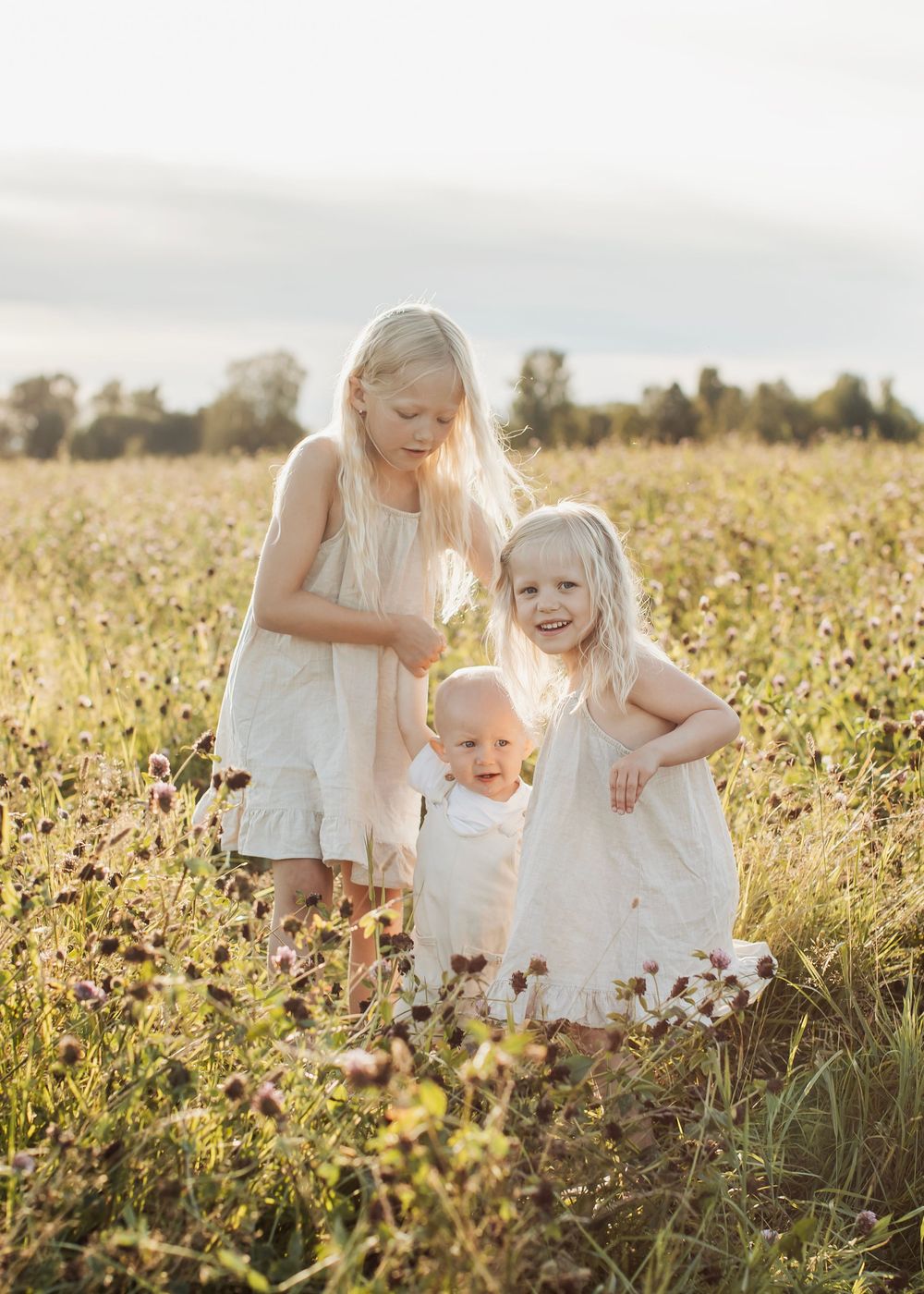Familjefotografering på en blomsteräng i Boden med tre syskon som går med varandra.