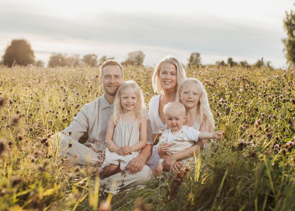 Family of five smiling together in a golden sunlit meadow, parents with three young children seated among wildflowers.