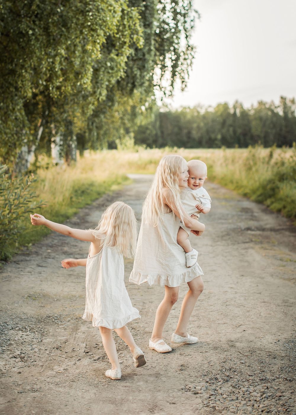 familjefotografering på sommaren på en skogsväg i Boden med tre syskon i matchande beiga färger som dansar