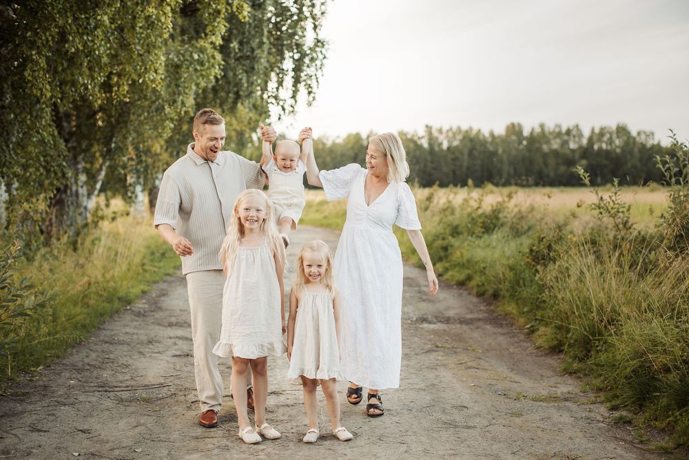 Happy family with three young daughters walking on a rural path surrounded by green fields on a sunny day.