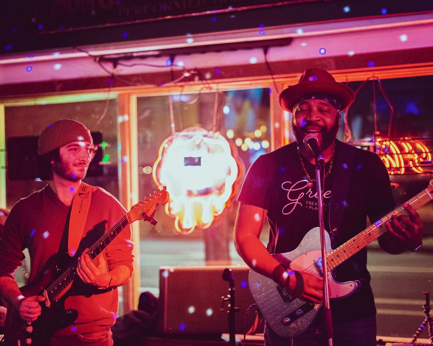 Musicians perform on stage under vibrant red lighting at a live music venue during an evening concert.