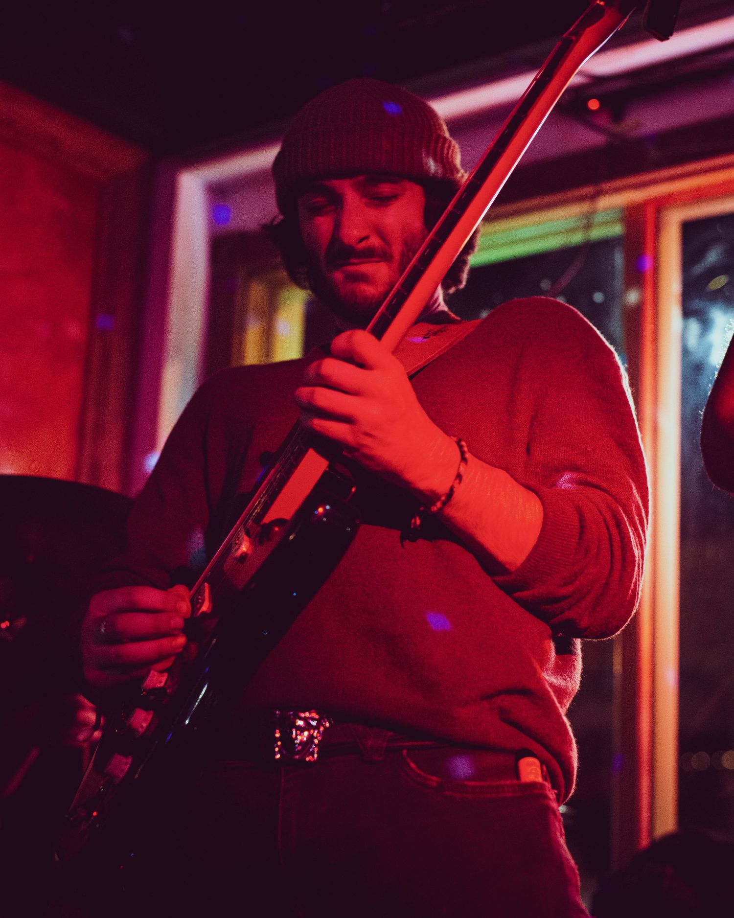 A musician plays violin under dramatic red stage lighting during a live performance.