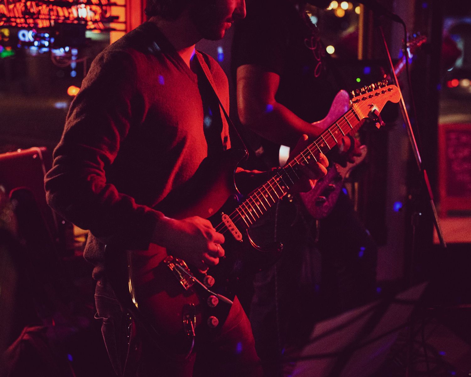 Musicians perform on stage in a dark venue illuminated by red lighting and spotlights.
