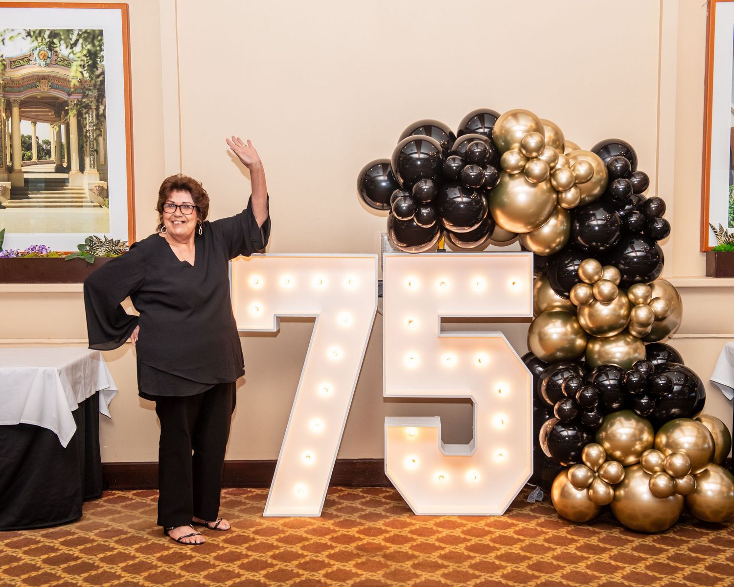 Black and gold balloon decorations and numbers create an elegant party display against a beige wall.