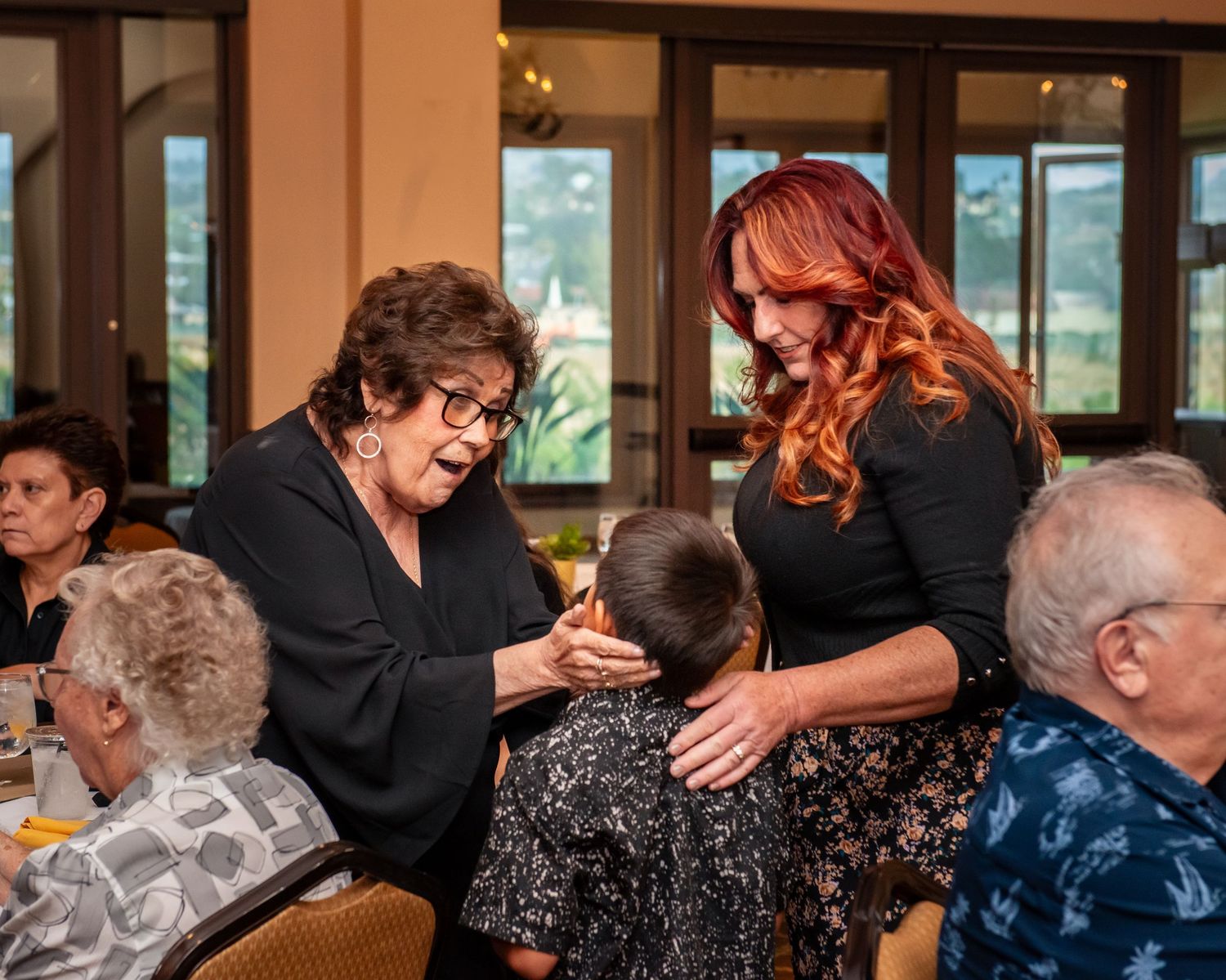 People celebrating at an indoor event with large windows overlooking a scenic view.