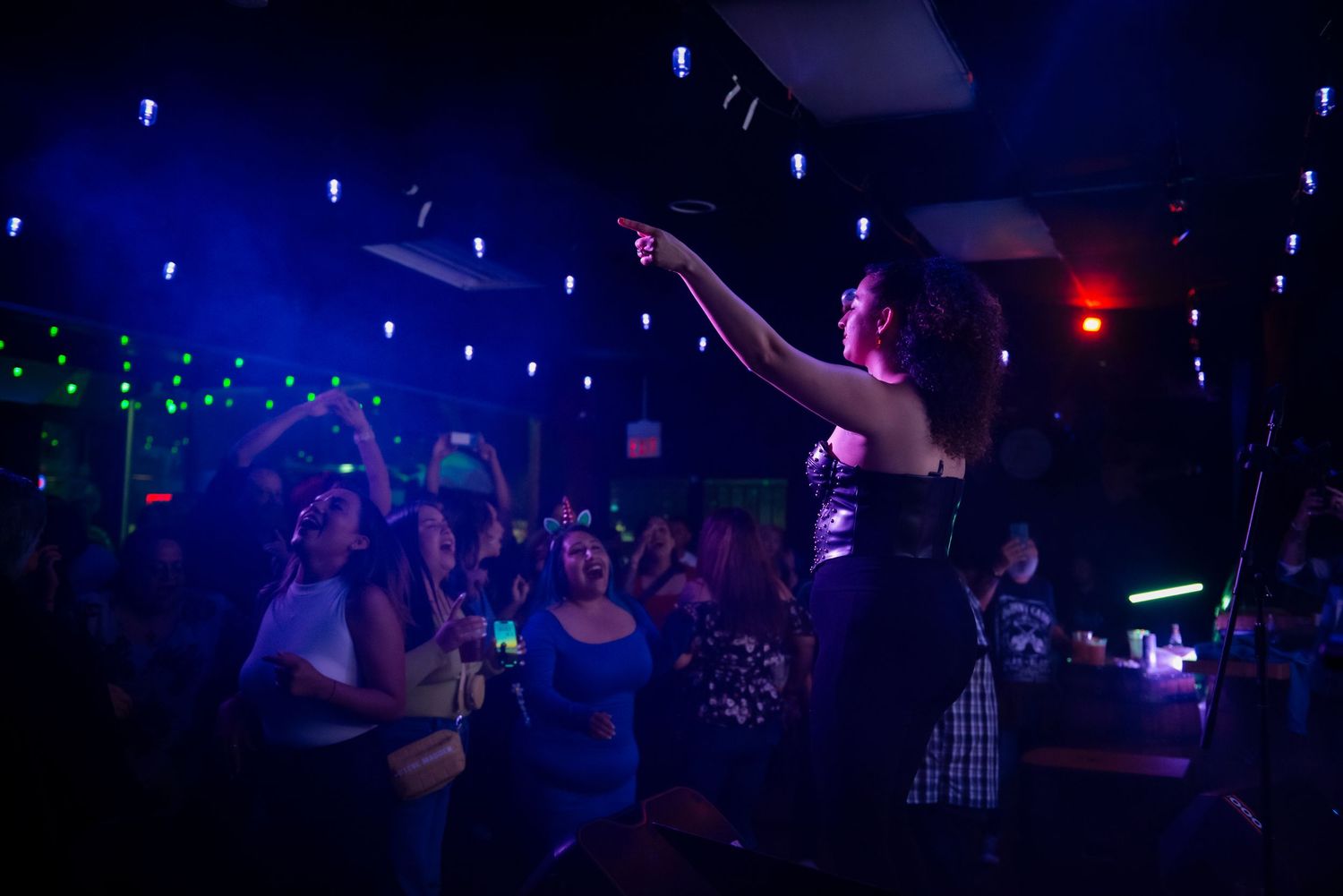 People dance and socialize in a dimly lit nightclub with blue lighting and glowing decorations.