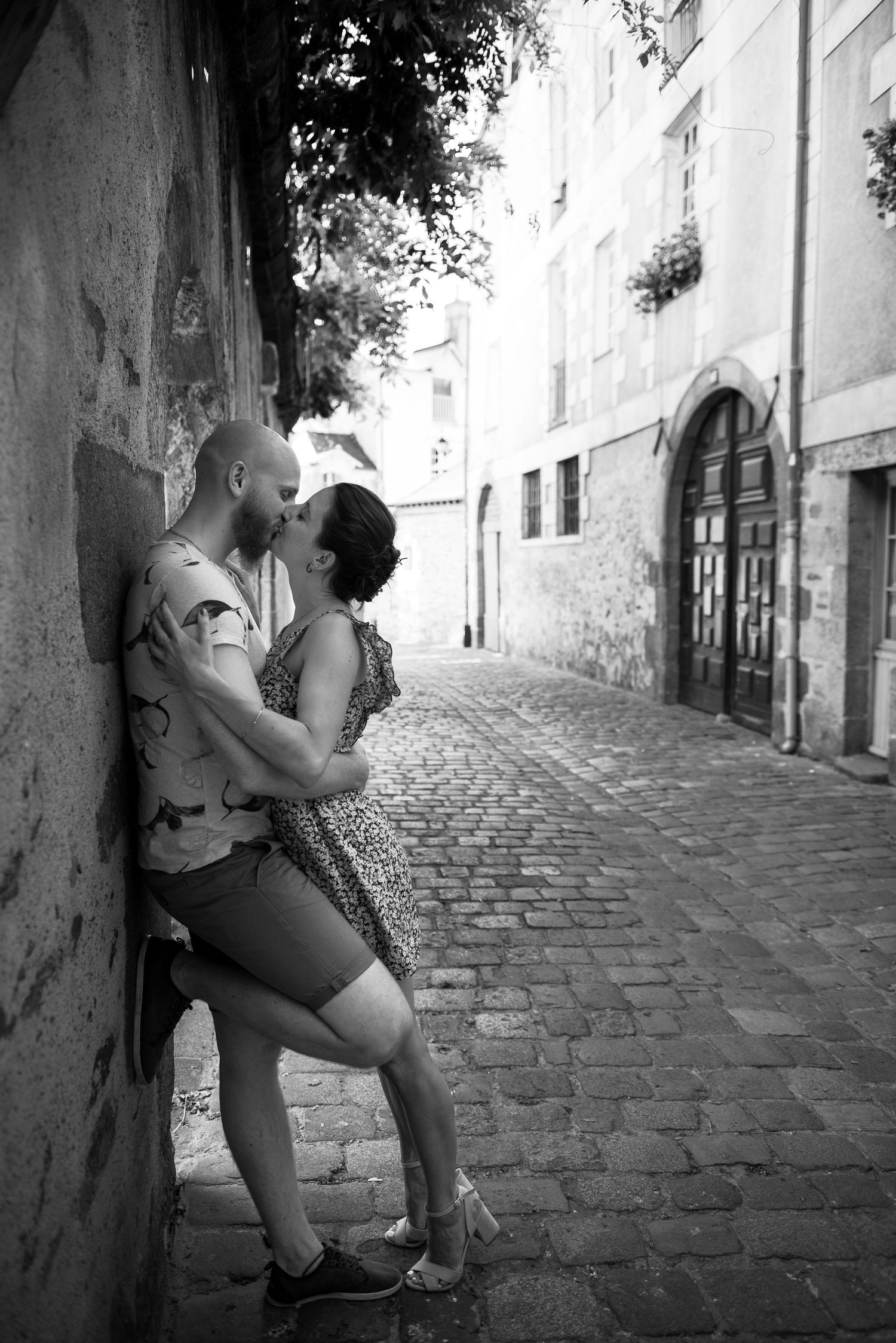 Couple enlacé dans une ruelle pavée en Bretagne, séance engagement romantique en noir et blanc.