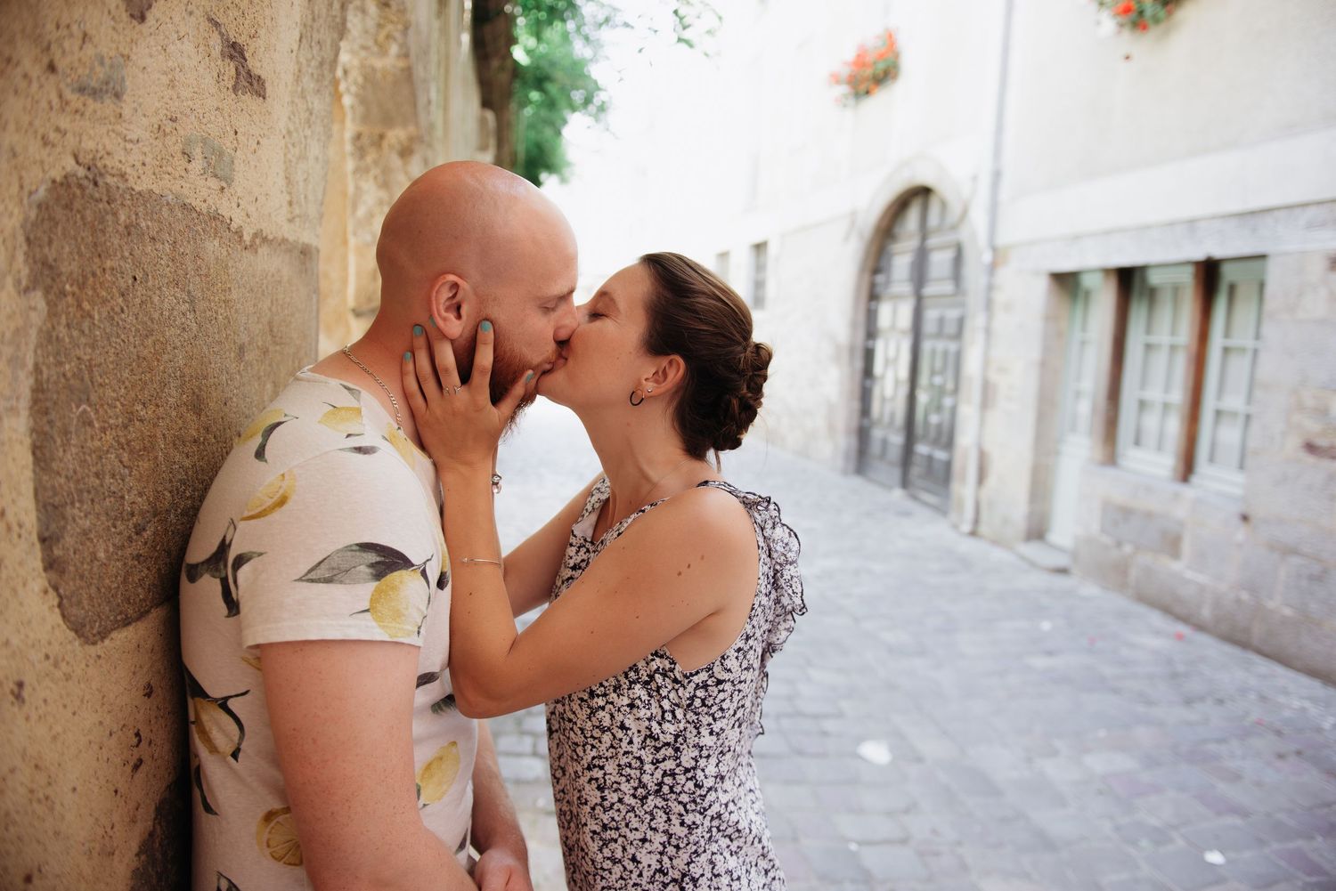 Couple s’embrassant contre un mur en pierre dans une ruelle bretonne, séance engagement romantique en lumière naturelle.