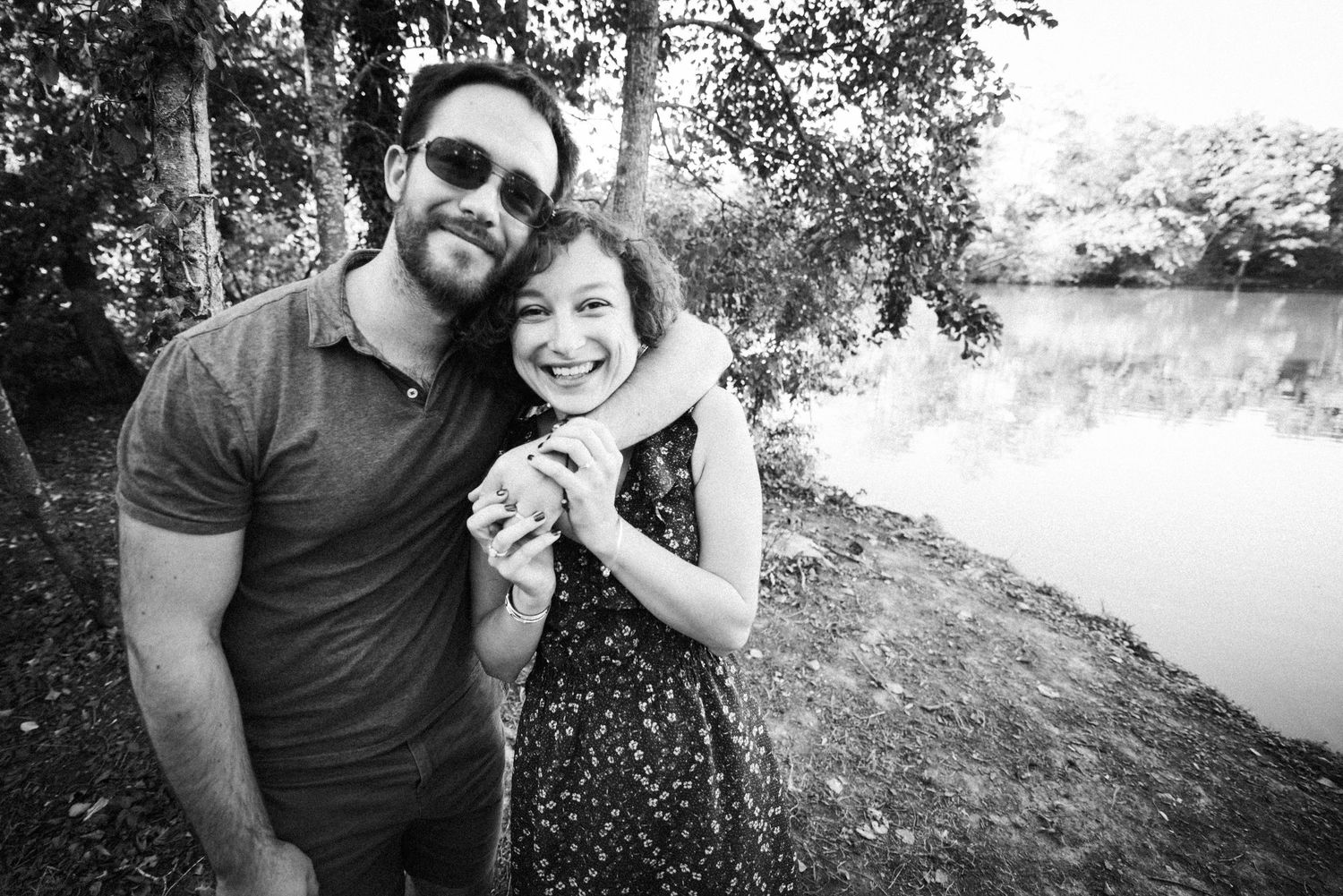 Couple souriant au bord d’un lac lors d’une séance engagement en Bretagne, photo en noir et blanc naturelle et spontanée.