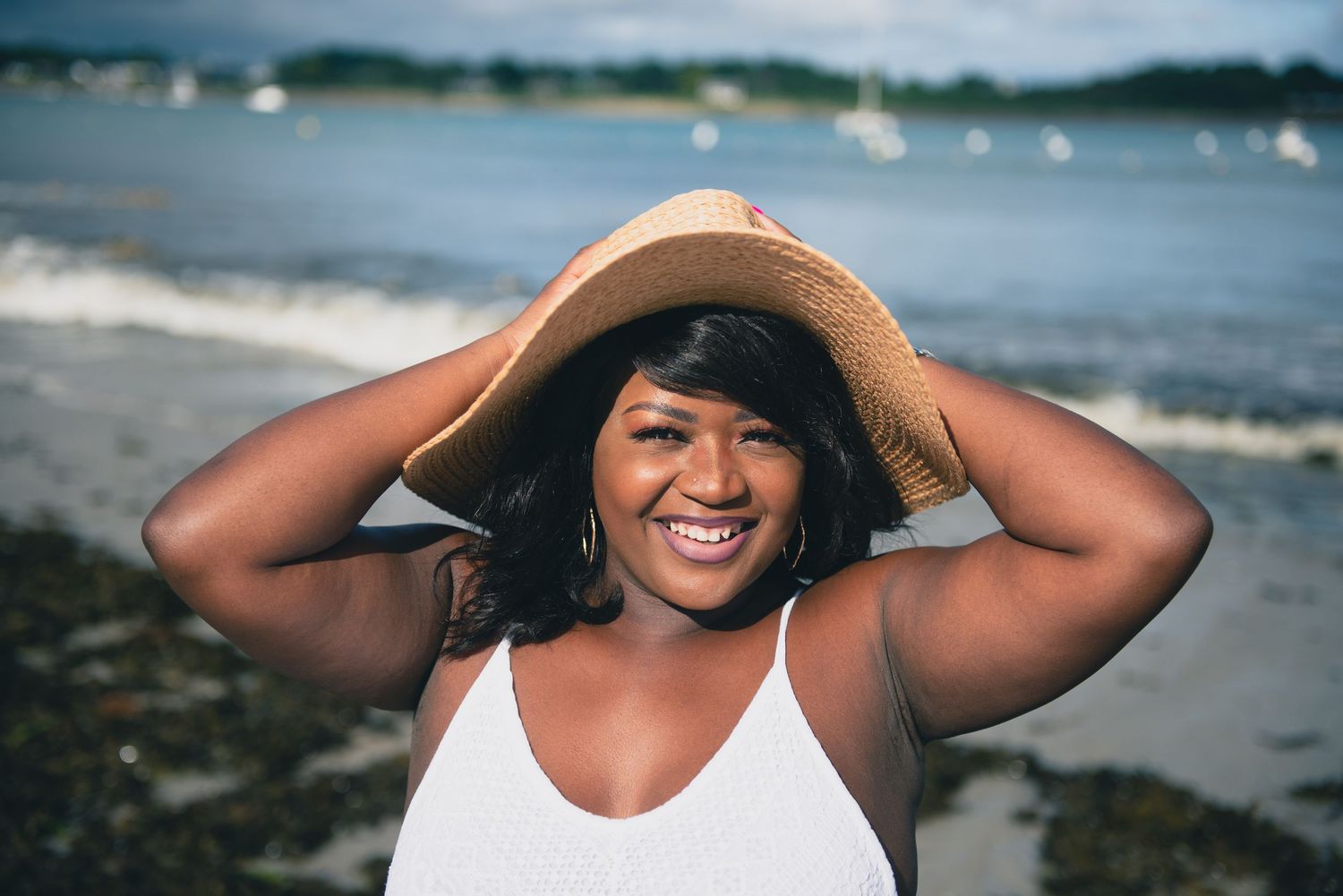 Portrait naturel d’une femme souriante avec chapeau sur une plage bretonne, séance photo couple en bord de mer.