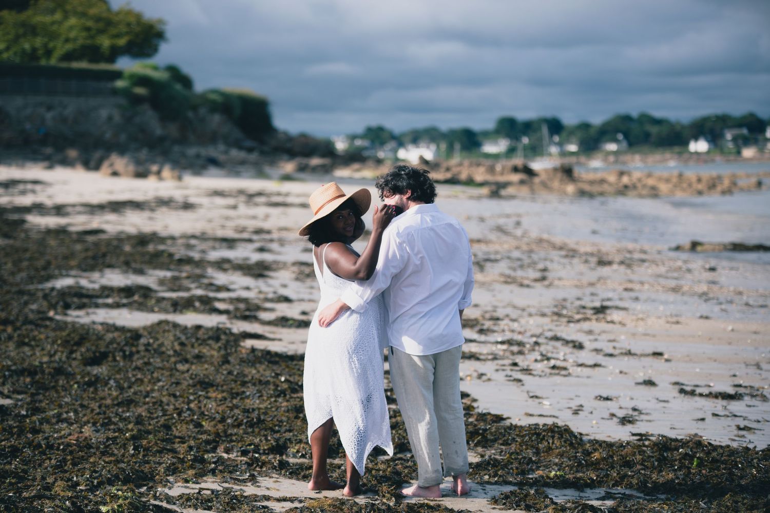 Couple marchant sur une plage rocheuse en Bretagne lors d’une séance engagement en bord de mer.