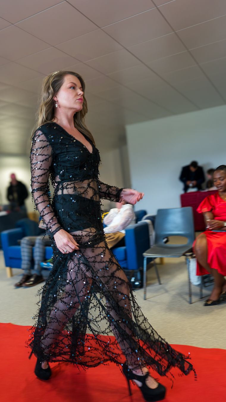 Dancer in flowing black lace dress performs dramatic spin movement on red carpet during indoor performance.