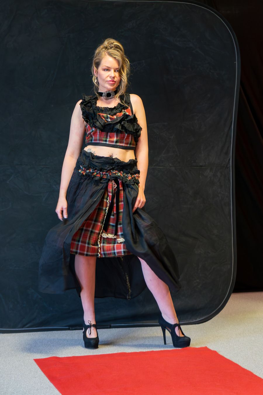 Model poses on red carpet wearing edgy punk-inspired outfit with plaid skirt, black crop top and platform heels.