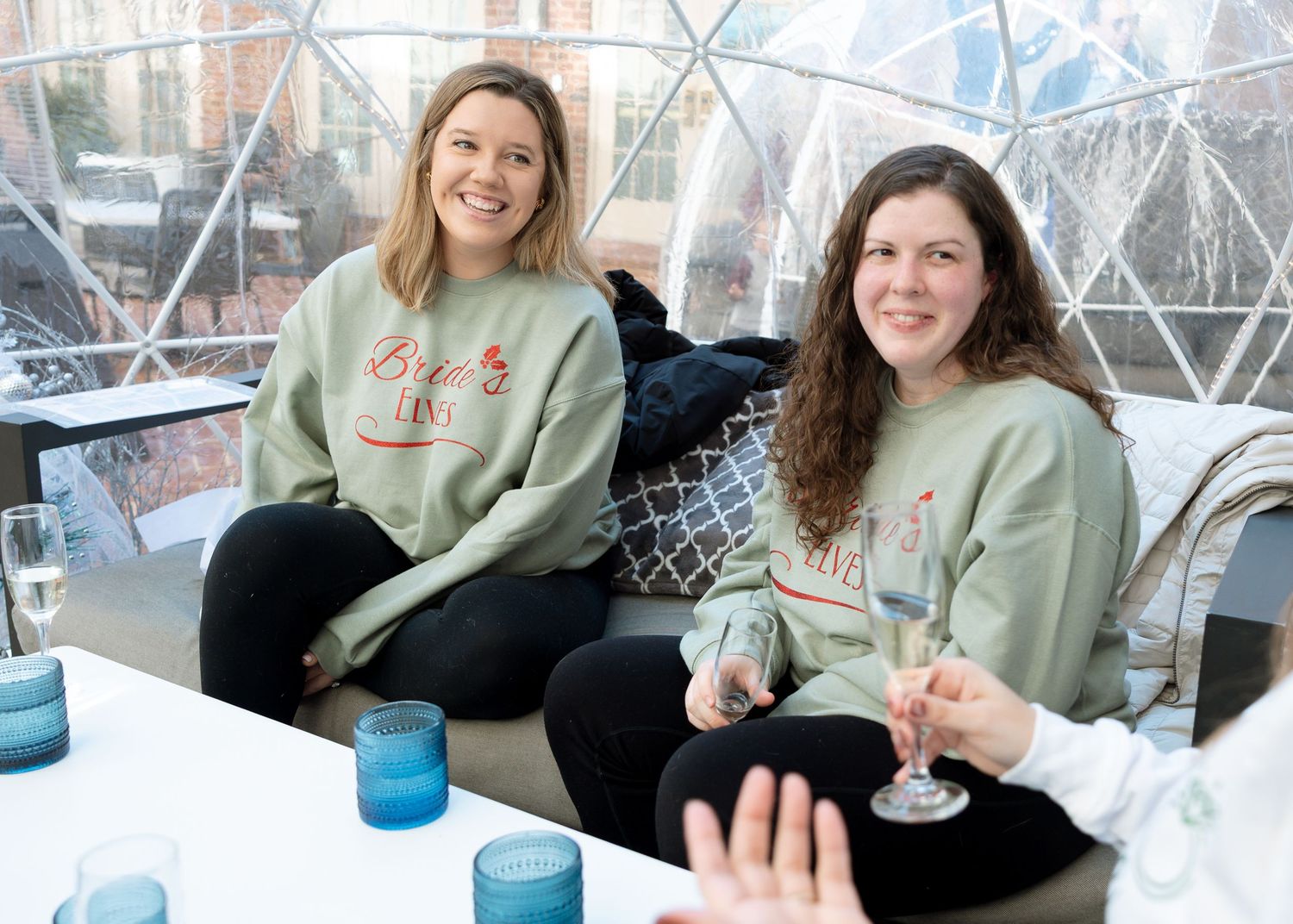 Bride surrounded by bridesmaids wearing matching sweatshirts — candid wedding celebration portrait