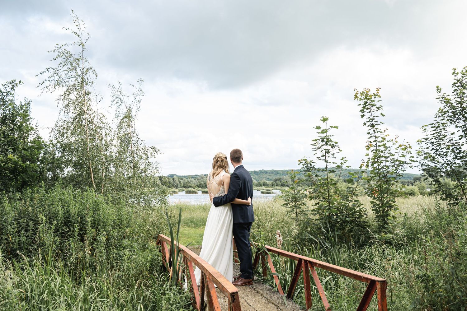 Worton Hall Wedding Photography with Bride and Groom photographed from behind as they look over the lake standing on a small red bridge