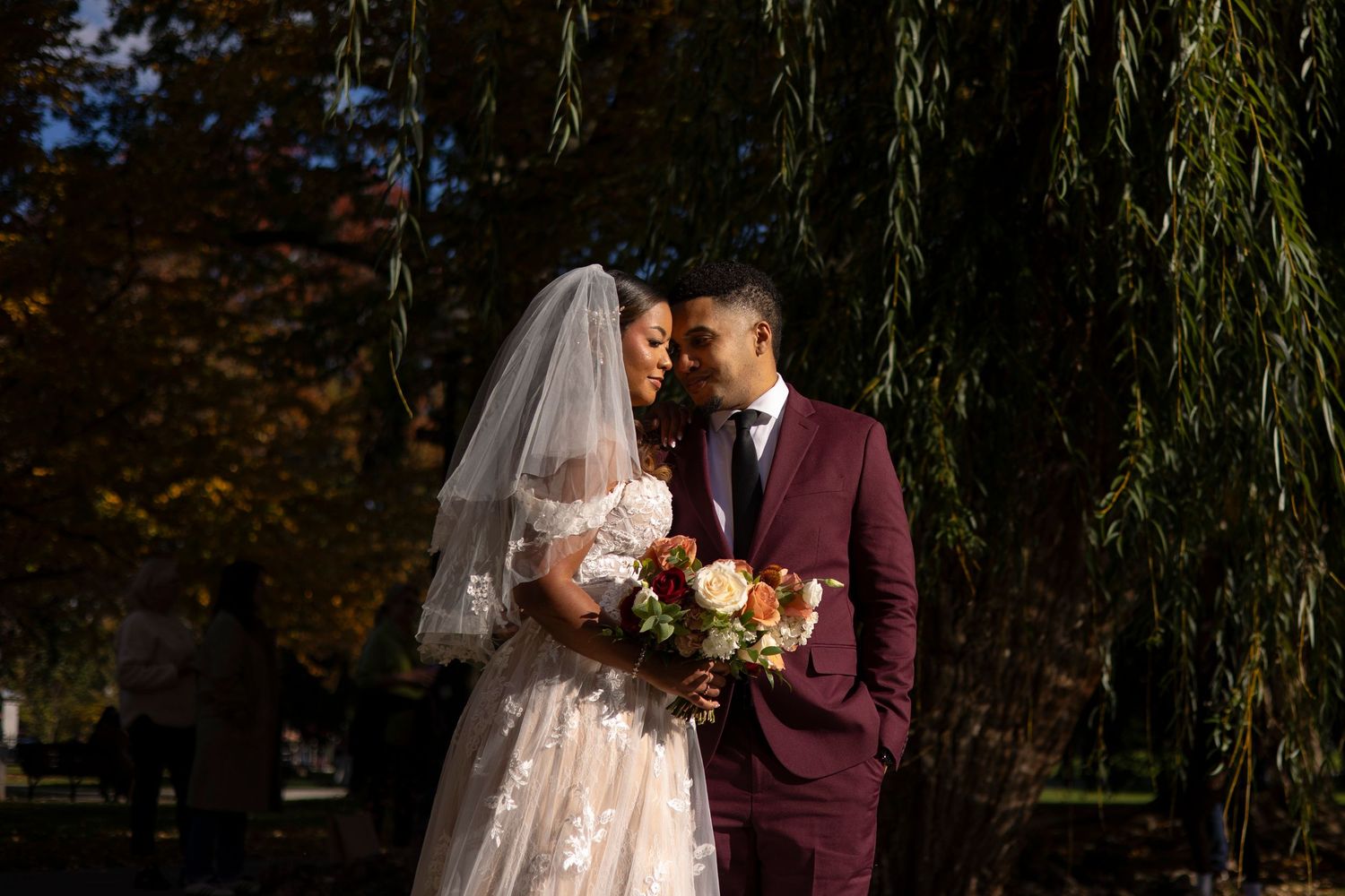 Newlywed couple shares romantic moments under a weeping willow tree in autumn wedding photos.