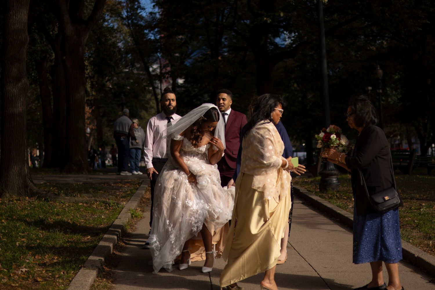 Wedding party in white dresses and formal attire walking through a park during golden hour.