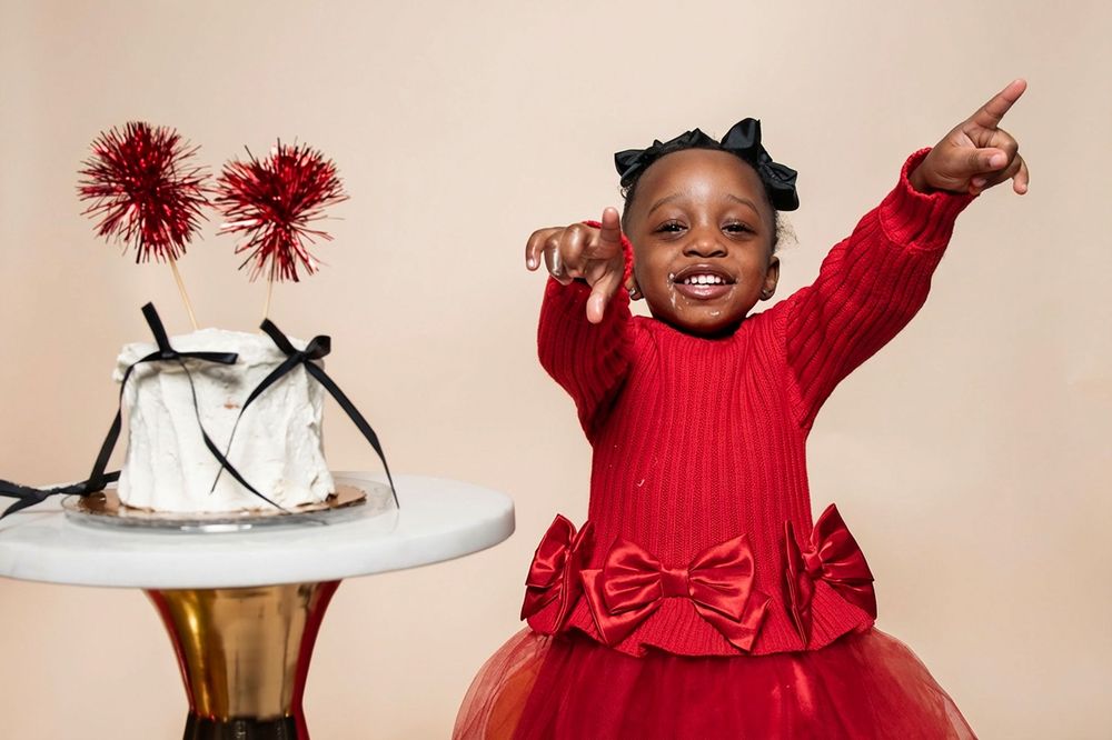 Joyful portrait of child in red tulle dress pointing upward near holiday decorations.