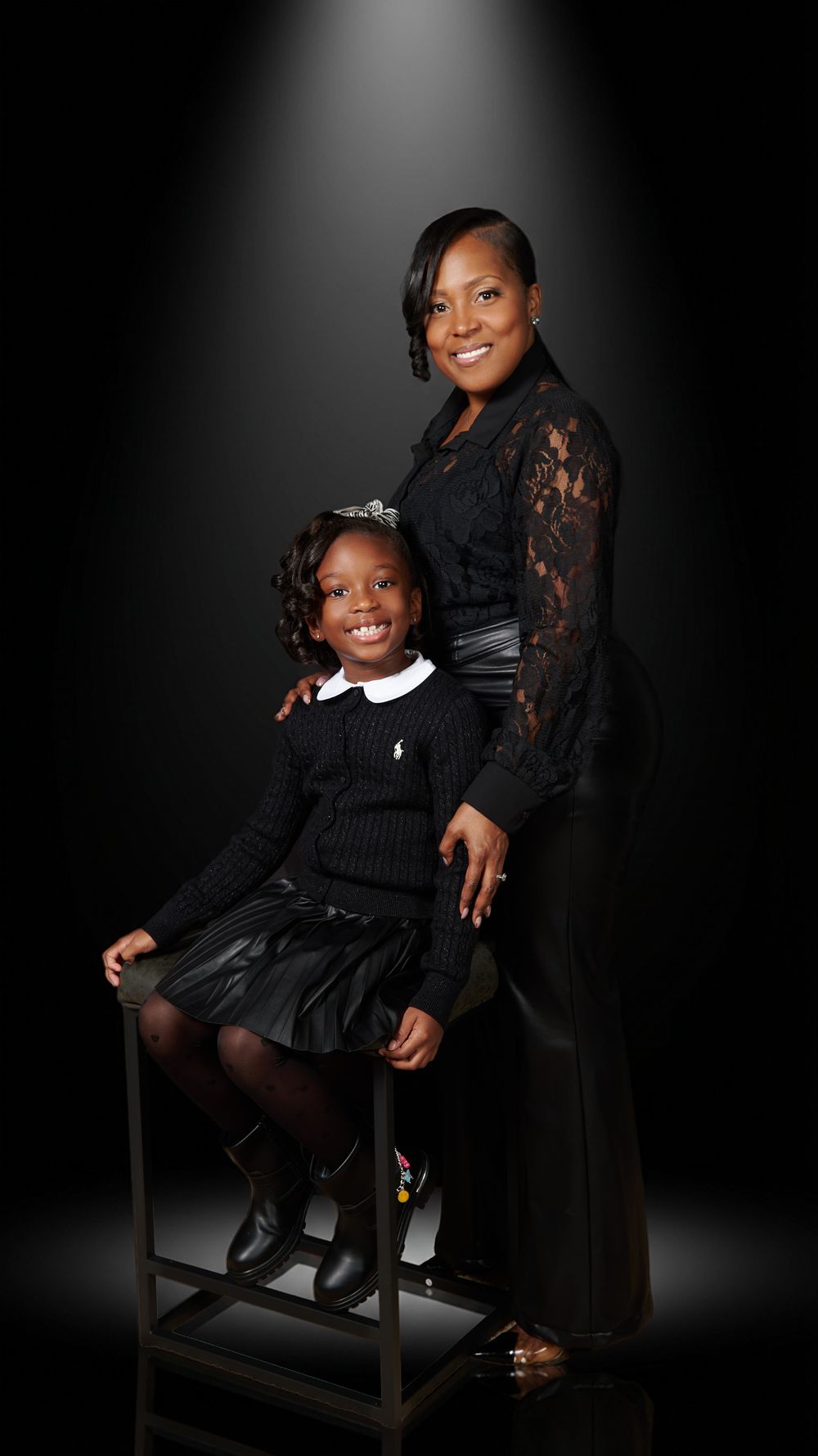 Studio portrait featuring two people in black formal attire against a dramatic dark background.