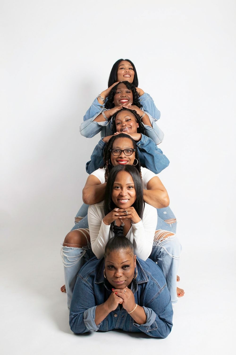 Playful pyramid pose of people in denim clothing against white background.
