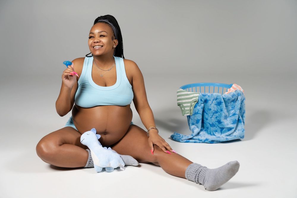 Person in light blue sports bra and shorts sits on floor with water bottle and blue tote bag against gray backdrop.