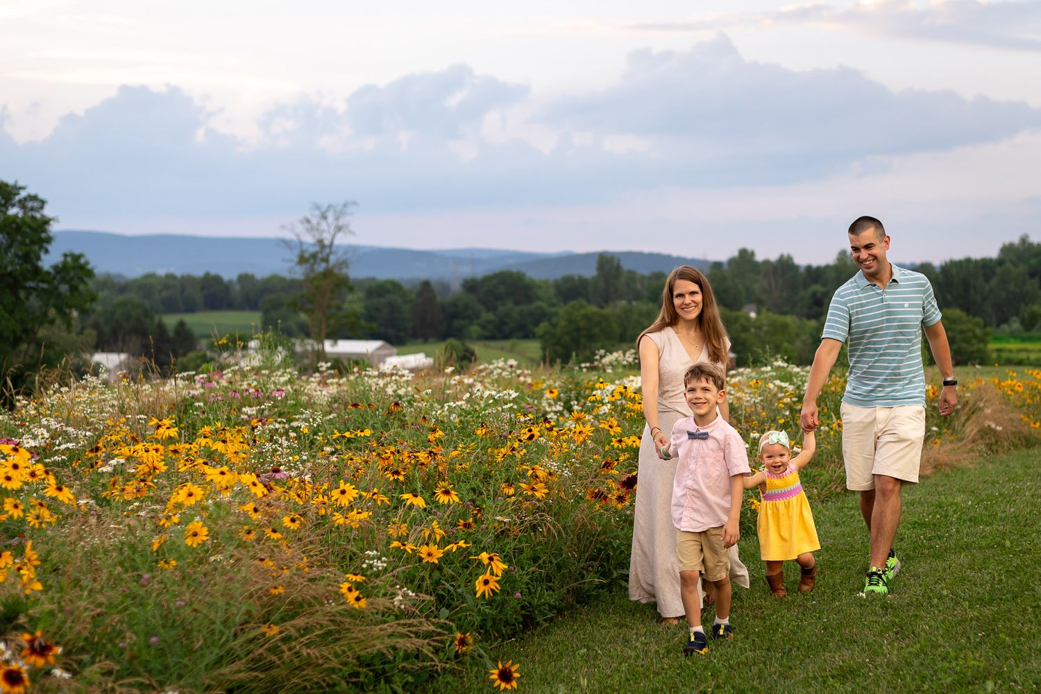A family walks together through vibrant yellow wildflower fields on a sunny summer day in the countryside.