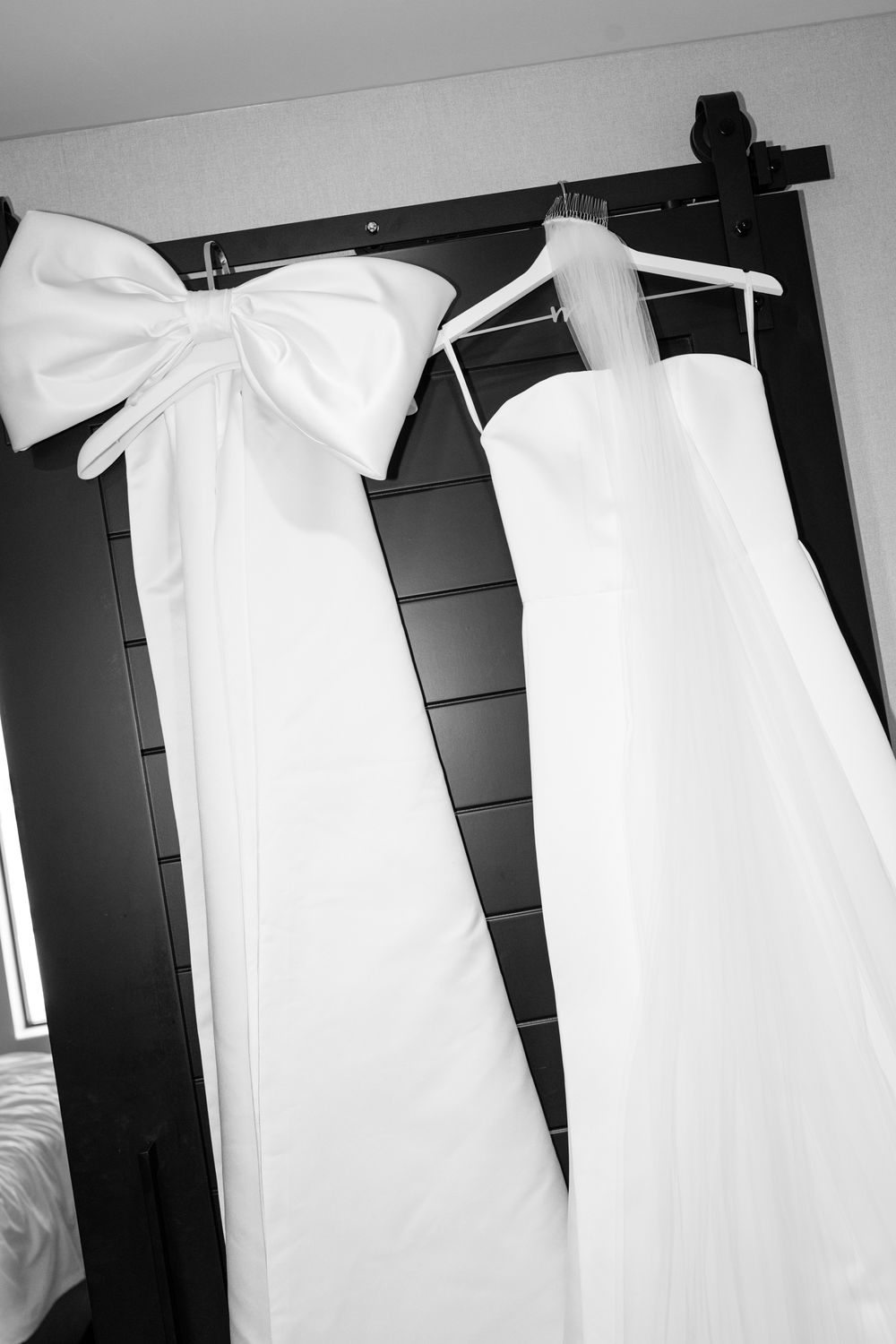 Row of white bridesmaid dresses hanging on black hangers against a dark wall.