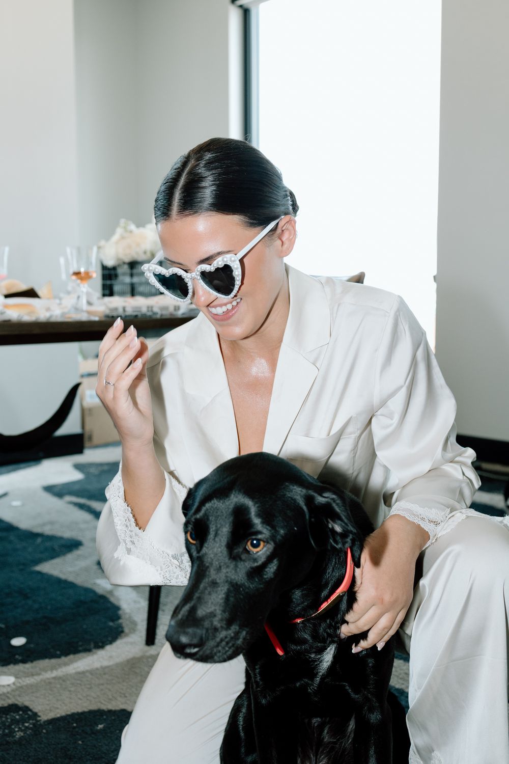 Person in white robe playing with black Labrador dog in bright interior room.